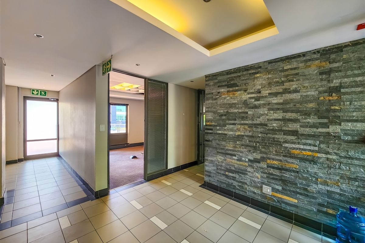 A modern office hallway featuring a decorative stone accent wall, recessed ceiling lighting, and tiled flooring leading into an adjacent office space.