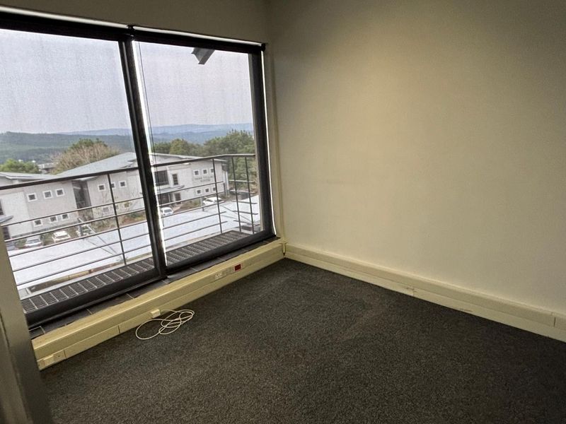 An empty office space featuring large windows with exterior views, carpeted flooring, and integrated perimeter trunking for electrical connectivity.