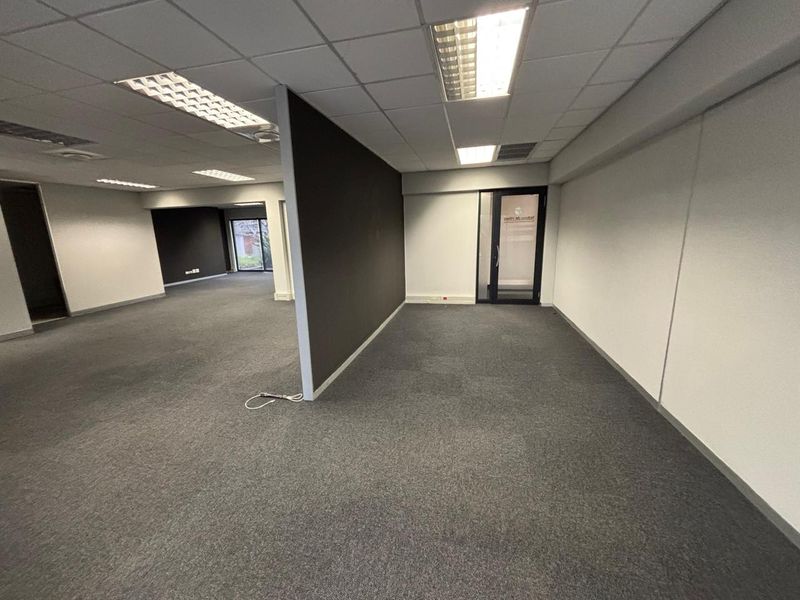 An open-plan office space featuring a neutral color palette, suspended ceilings with recessed lighting, and carpeted flooring, offering a versatile workspace layout.