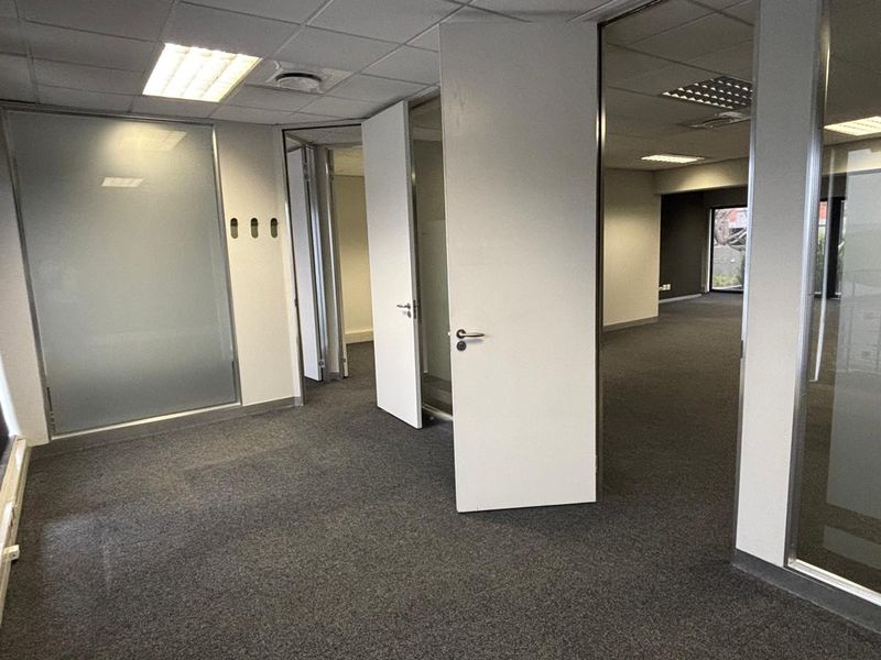 A vacant office space featuring carpeted flooring, suspended ceilings with recessed lighting, and glass partition walls creating multiple work areas.