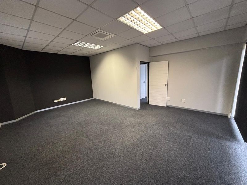A clean, empty office space featuring a suspended ceiling with recessed lighting, grey carpeting, and neutral wall finishes, ready for professional use.