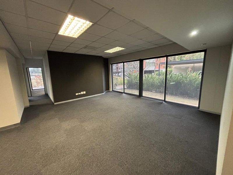 Spacious, empty office area featuring large sliding glass doors, carpeted flooring, and a suspended ceiling with recessed lighting.