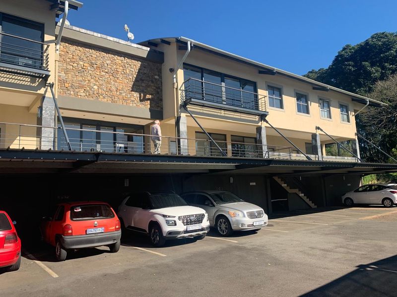 Front elevation of a multi-story office building featuring stone cladding, metal balcony railings, and a covered ground-level parking area.