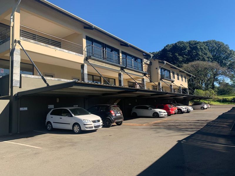 Exterior view of a multi-story office building featuring covered parking bays on the ground level and private balconies on the upper floors.