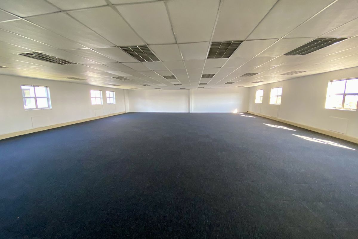 A spacious, open-plan office area featuring a suspended grid ceiling with integrated lighting and dark carpeting throughout.