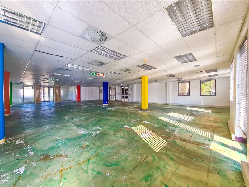 A large, open-plan office space featuring a suspended ceiling, recessed lighting, and structural columns, currently requiring floor refurbishment.