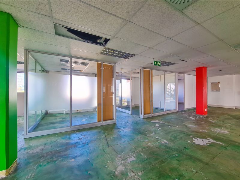 Open plan office space featuring glass partitioned rooms, suspended ceilings, and worn flooring, requiring refurbishment to restore professional functionality.