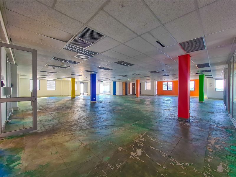 A large, open-plan office space featuring a suspended ceiling, recessed lighting, and multiple structural columns, currently requiring floor refurbishment.