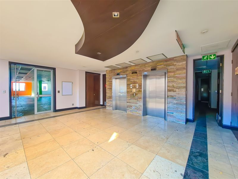 Spacious office building lobby featuring stone-clad elevator banks, modern recessed ceiling design, and polished tile flooring with glass entry doors.