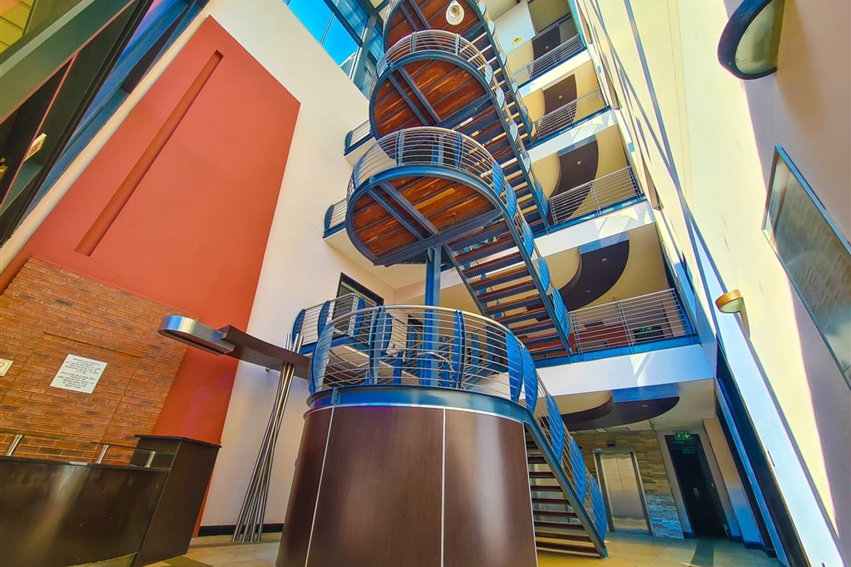 Spacious office building atrium featuring a prominent spiral staircase, high ceilings with skylights, and modern architectural finishes including brick and stone elements.