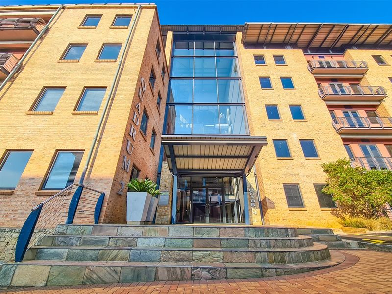 Front elevation of a multi-story office building featuring a prominent glass atrium entrance, brick facade, and stone staircase access.
