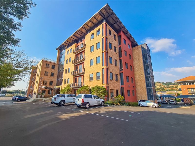 A multi-story office building featuring a brick and glass facade, metal roofing, and dedicated surface parking.
