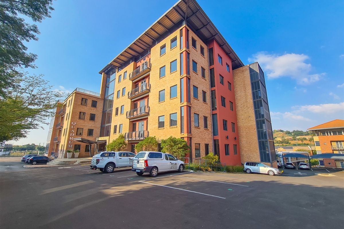 A multi-story office building featuring a brick and glass facade, metal roofing, and dedicated surface parking.