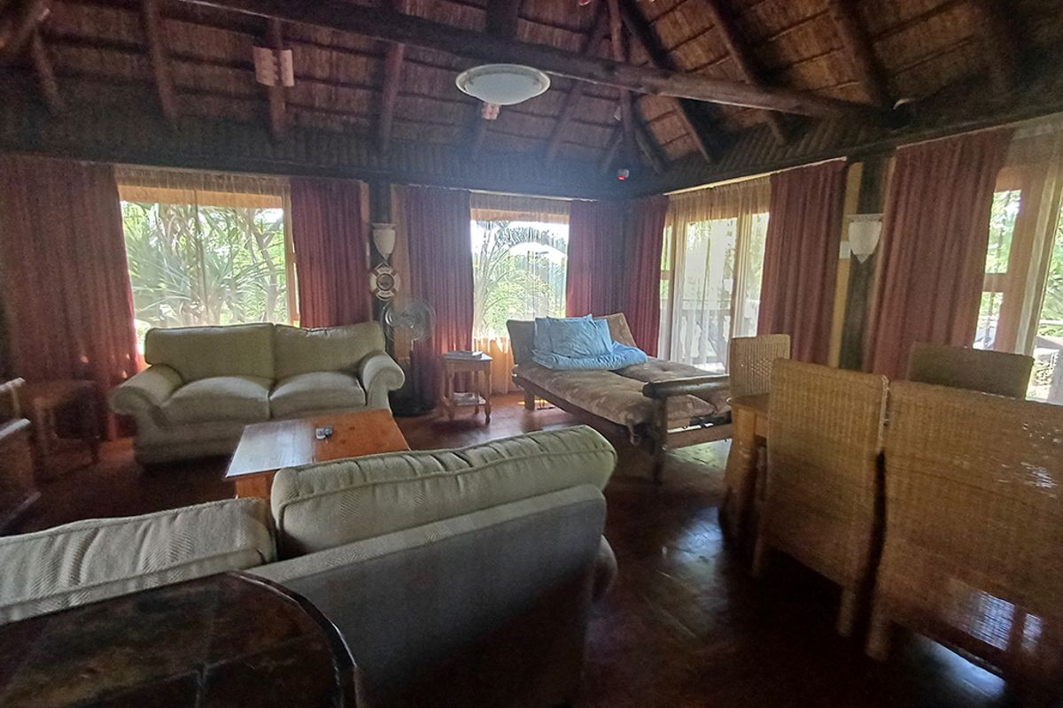 Spacious living area featuring a traditional thatched roof with exposed timber beams, wooden flooring, and large glass sliding doors providing natural light.