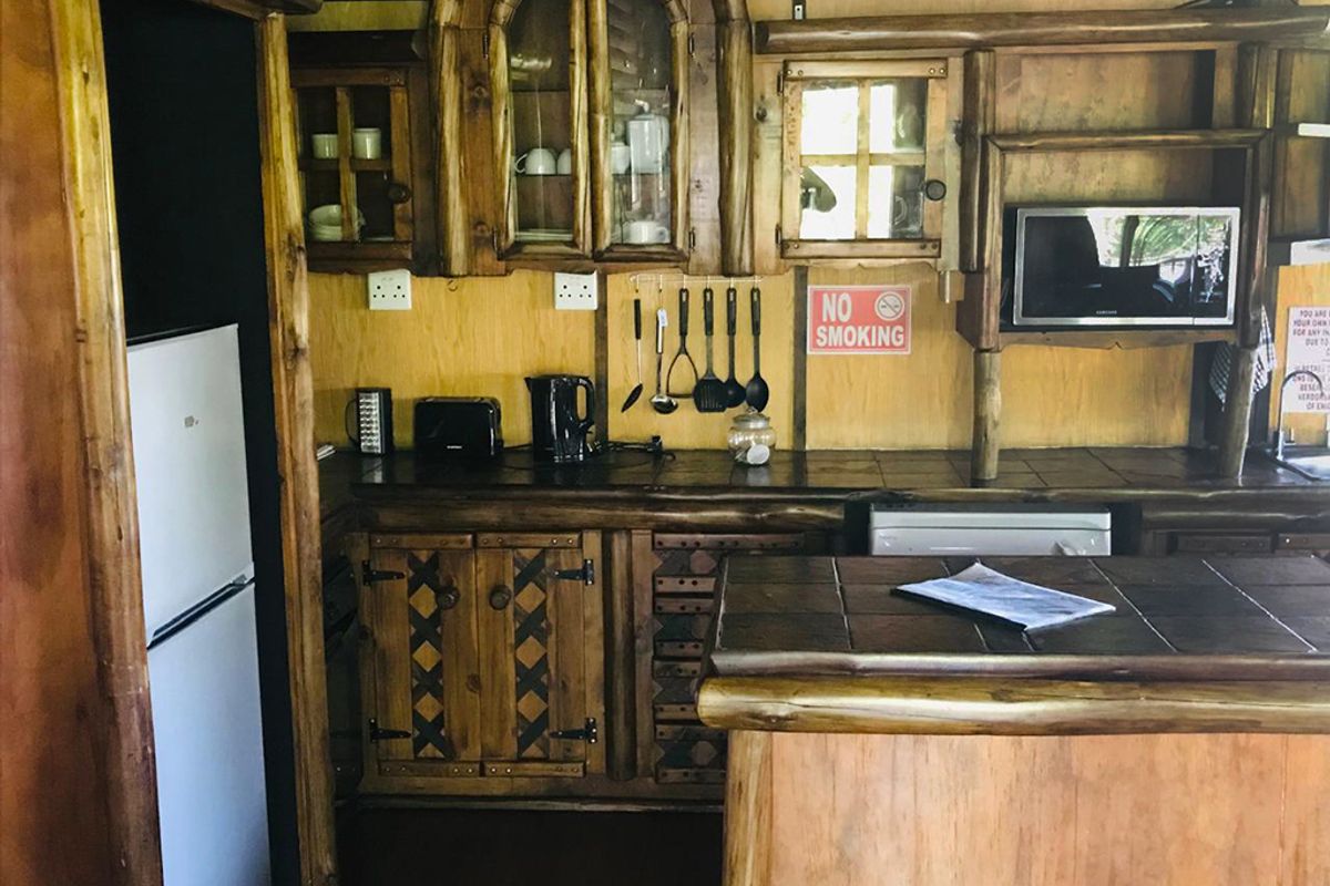 Rustic kitchen featuring custom wooden cabinetry, tiled countertops, and a breakfast bar, offering a traditional guest house aesthetic.