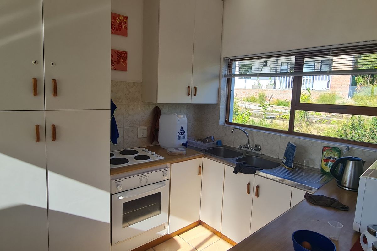A functional kitchen featuring white built-in cabinetry, an electric hob, an integrated oven, and a double sink with a window view.