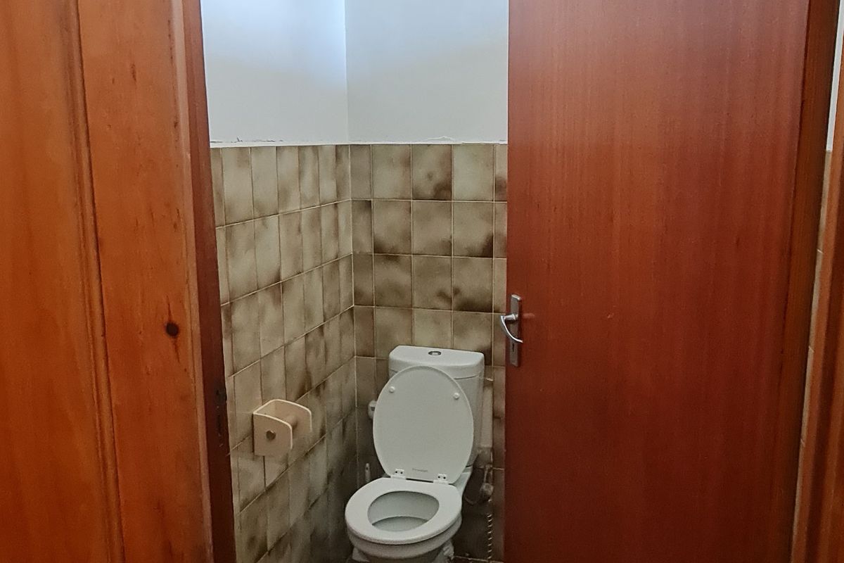 A small, functional bathroom featuring a toilet, tiled finishes, and an overhead electric water heater unit.