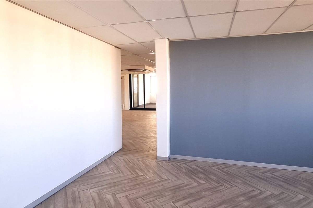 A bright, open-plan office space featuring modern herringbone-patterned flooring, a suspended acoustic ceiling, and a clean, neutral color palette.