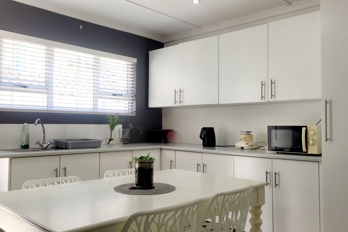 A clean, functional kitchen featuring white cabinetry, laminate countertops, a stainless steel sink, and a window with fitted blinds.