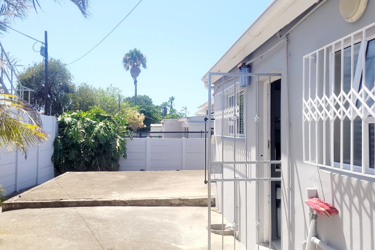 A rear exterior view featuring a concrete patio area, security gates on windows, and a perimeter wall in a residential setting.
