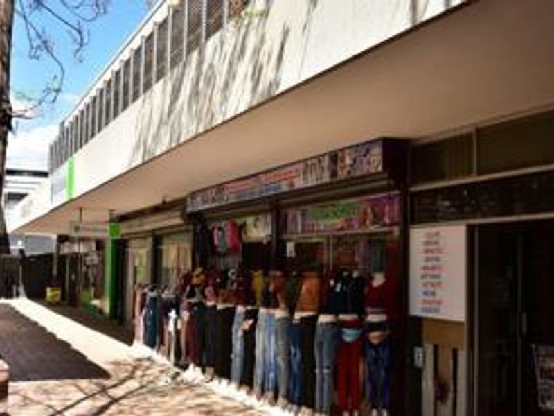 A commercial storefront featuring a covered walkway, glass display windows, and metal security shutters, typical of a retail strip center.