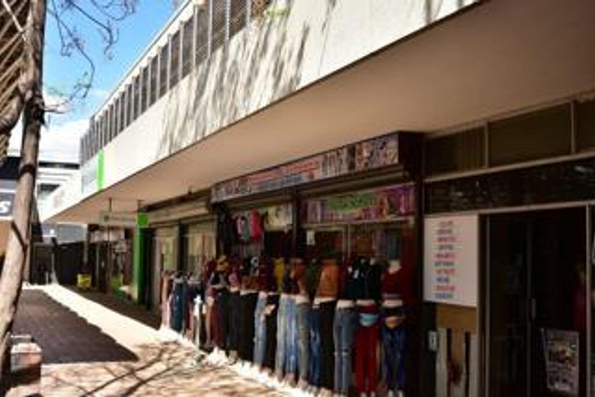 A commercial storefront featuring a covered walkway, glass display windows, and metal security shutters, typical of a retail strip center.