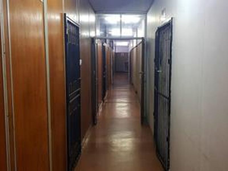 A long commercial hallway featuring wood-paneled walls, vinyl flooring, and multiple security gates leading to individual units.