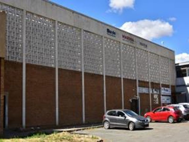 Exterior view of a commercial building featuring a brick and breeze block facade with an adjacent asphalt parking area.