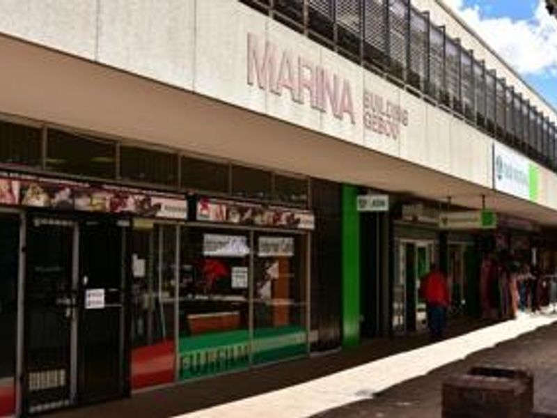 Street-level view of the Marina Building commercial storefront featuring glass display windows and a covered pedestrian walkway.