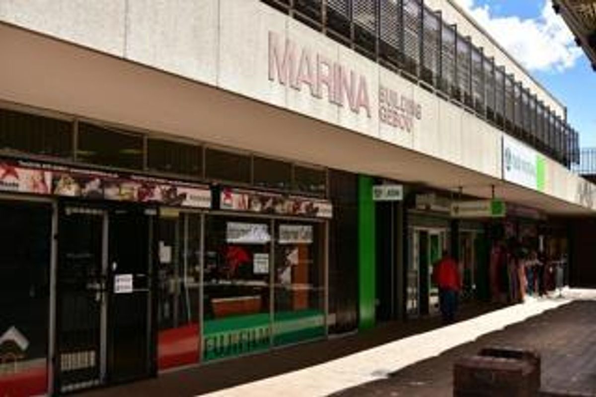Street-level view of the Marina Building commercial storefront featuring glass display windows and a covered pedestrian walkway.