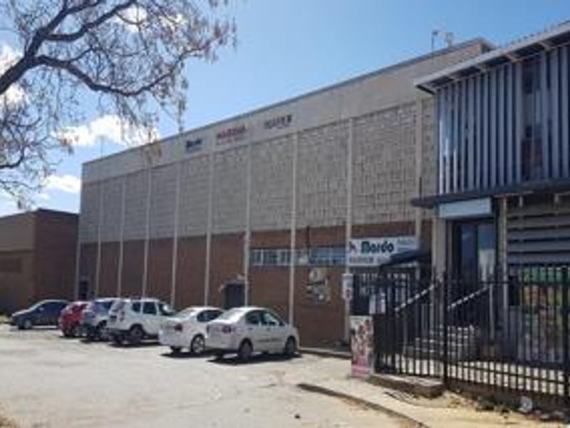 Front exterior view of a commercial building featuring a brick and breeze block facade with an adjacent asphalt parking area and security fencing.