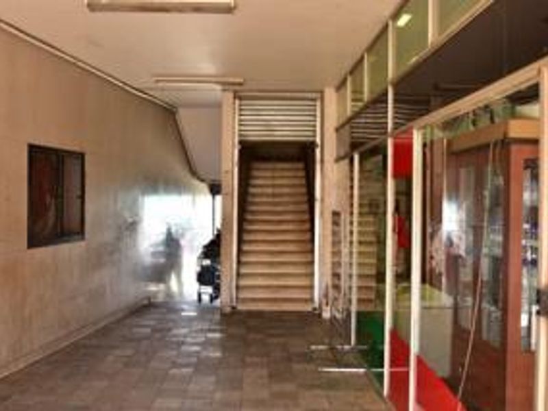 A commercial hallway featuring tiled flooring, fluorescent lighting, and a staircase leading to an upper level, with glass storefront access to the side.