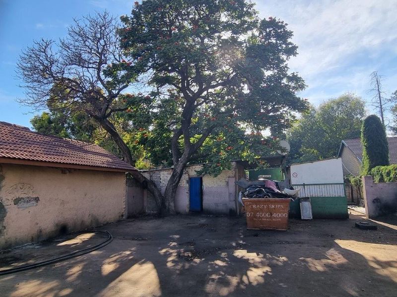 Rear exterior area featuring a paved yard, boundary walls, and a tiled roof structure, showing signs of significant wear and maintenance requirements.