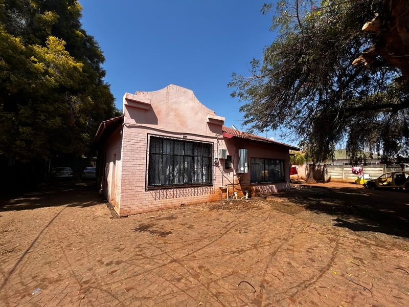 Front view of a single-story brick building featuring security bars on windows and a paved driveway area.