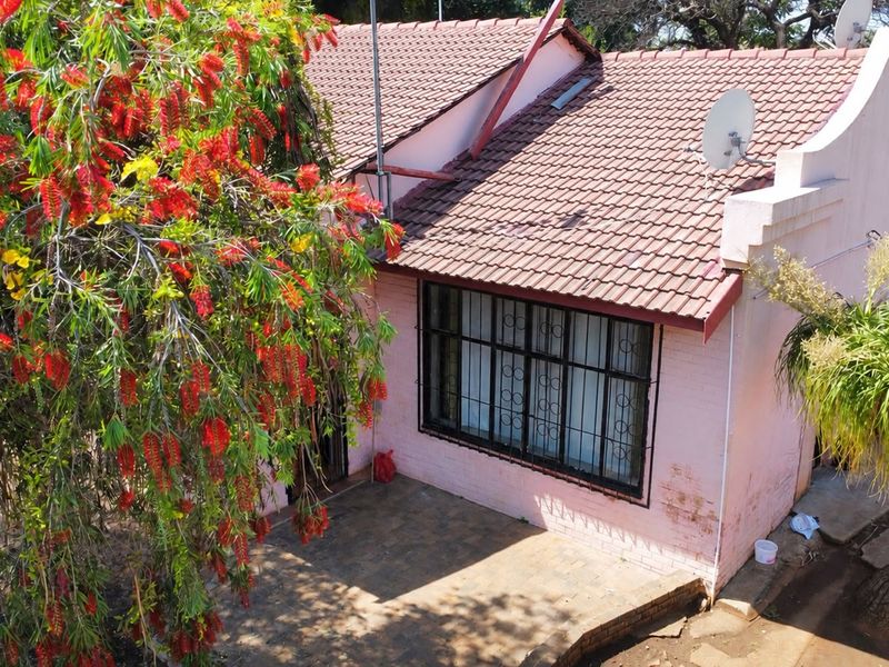 Rear exterior view of the property featuring a tiled roof, paved patio area, and security-fitted windows, surrounded by established garden greenery.