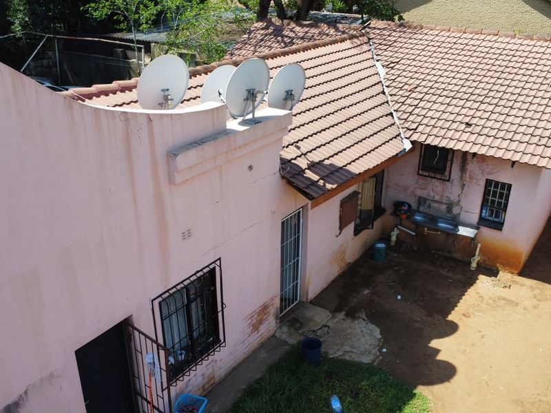 Aerial view of the rear exterior showing a tiled roof, multiple satellite dishes, security bars on windows, and an external utility sink area.