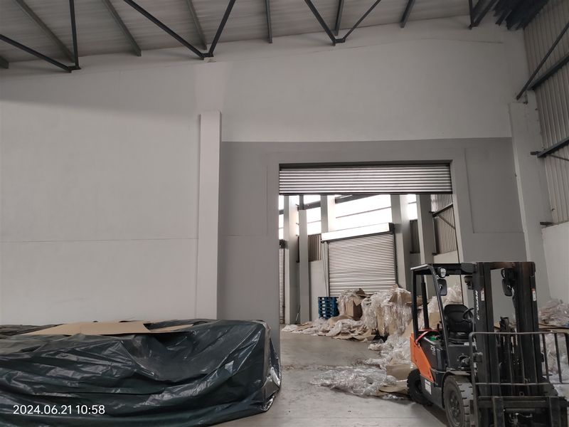 Industrial warehouse space featuring high ceilings with exposed steel trusses, concrete flooring, and multiple roller shutter doors for efficient access.