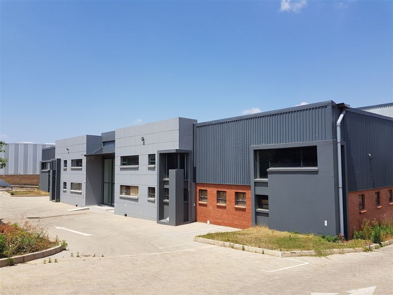 Modern industrial building featuring a combination of grey metal cladding and red brick facade with a paved driveway and landscaped areas.
