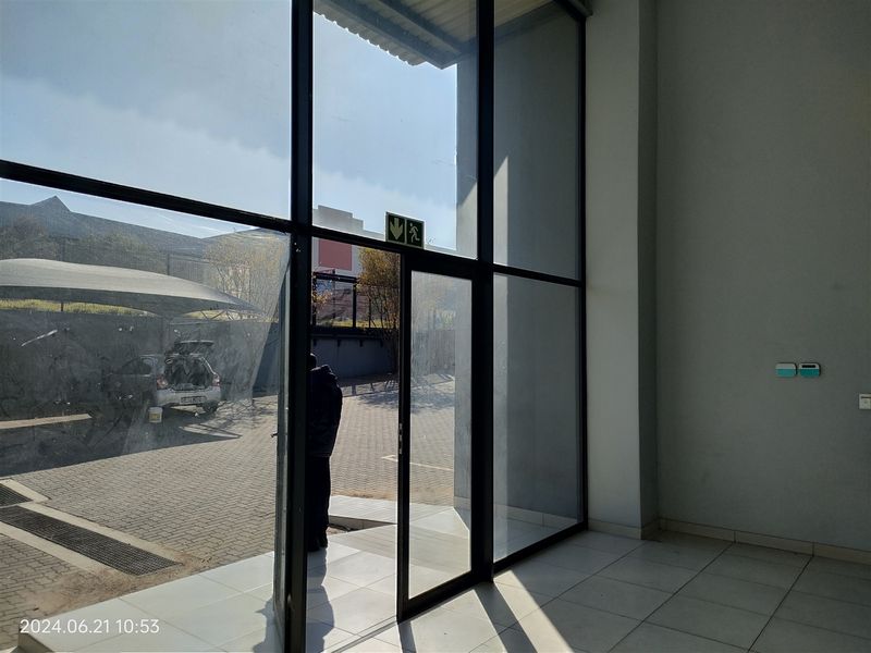 Bright industrial entrance area featuring large floor-to-ceiling glass panels, aluminum framing, and clean tiled flooring with direct access to the exterior parking area.