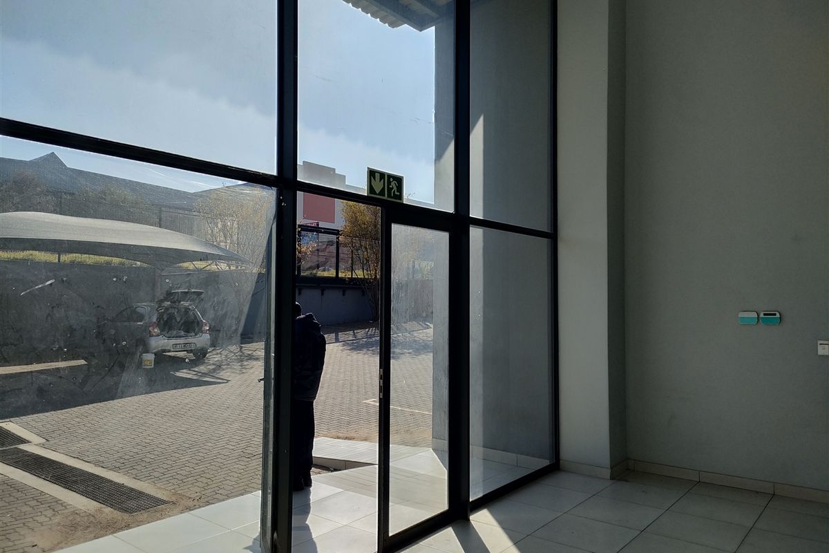 Bright industrial entrance area featuring large floor-to-ceiling glass panels, aluminum framing, and clean tiled flooring with direct access to the exterior parking area.