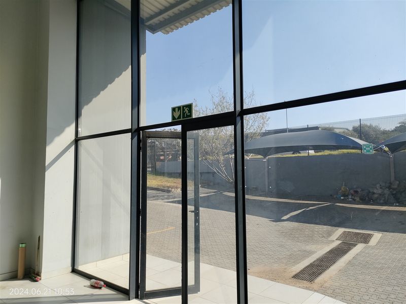 Bright industrial entrance area featuring expansive floor-to-ceiling glass panels, aluminium framing, and clean tiled flooring with direct access to the exterior parking area.