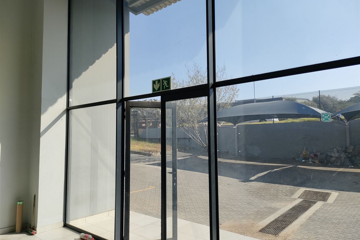 Bright industrial entrance area featuring expansive floor-to-ceiling glass panels, aluminium framing, and clean tiled flooring with direct access to the exterior parking area.