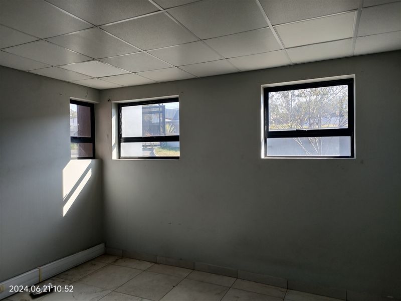 An empty office space featuring a suspended ceiling, tiled flooring, and multiple aluminium-framed windows providing natural light.