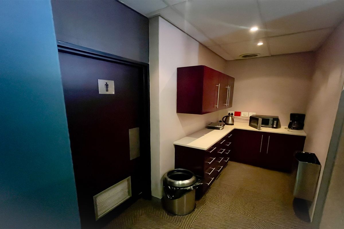 A functional office kitchenette area featuring built-in cabinetry, countertop space, and direct access to a restroom facility.
