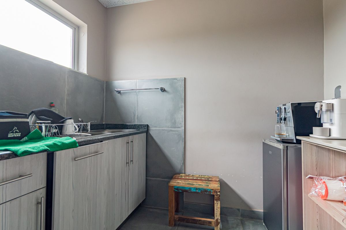 A functional kitchenette area featuring built-in cabinetry, a granite countertop, a stainless steel sink, and tiled splashbacks.