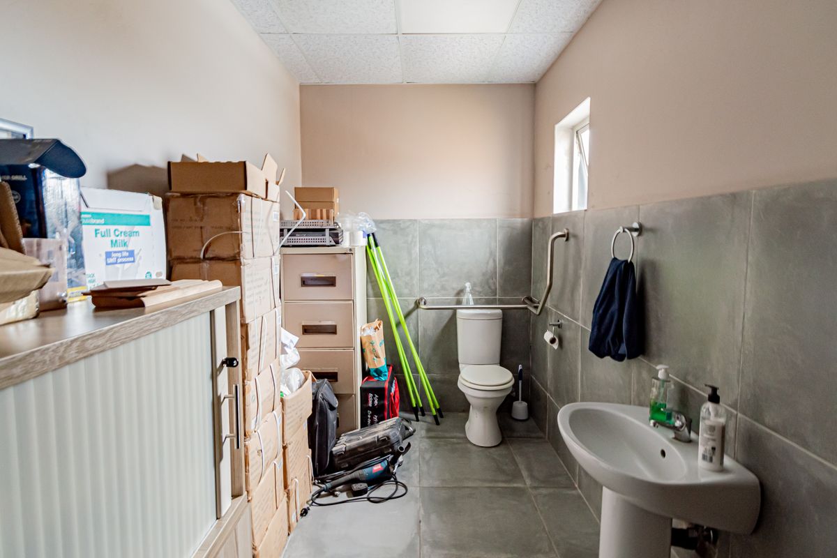 A functional industrial bathroom featuring a pedestal basin, toilet with grab rails, and tiled wall finishes.