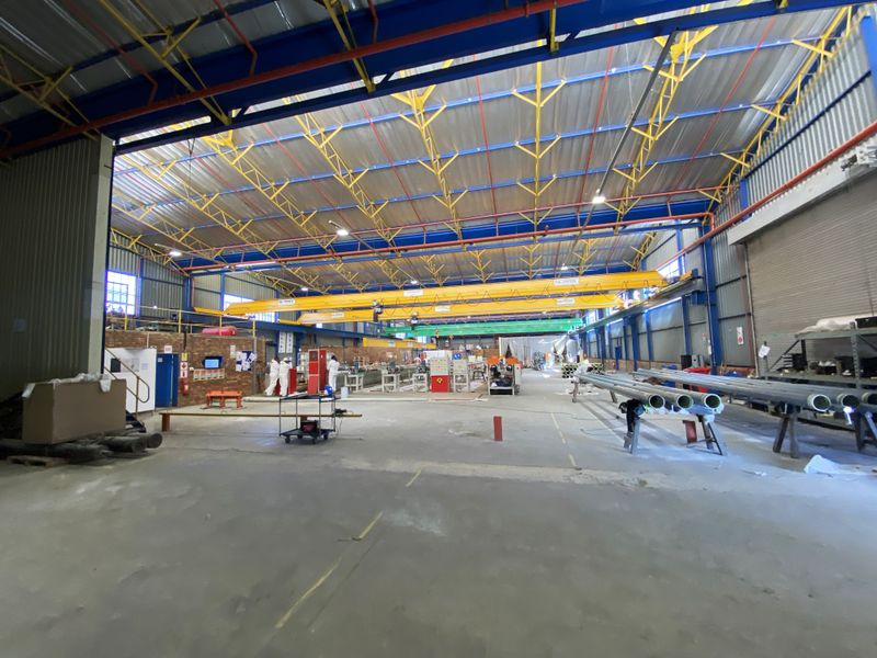 Spacious industrial warehouse facility featuring high ceilings with exposed steel trusses, overhead gantry cranes, and durable concrete flooring suitable for manufacturing or storage operations.