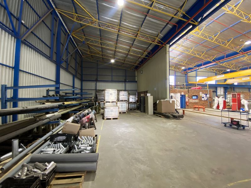 Spacious industrial warehouse featuring high ceilings with exposed steel trusses, concrete flooring, and an integrated overhead gantry crane system.
