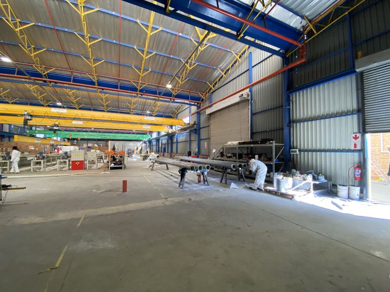 Spacious industrial warehouse facility featuring high-clearance steel truss roofing, overhead gantry cranes, concrete flooring, and large roller shutter access doors.