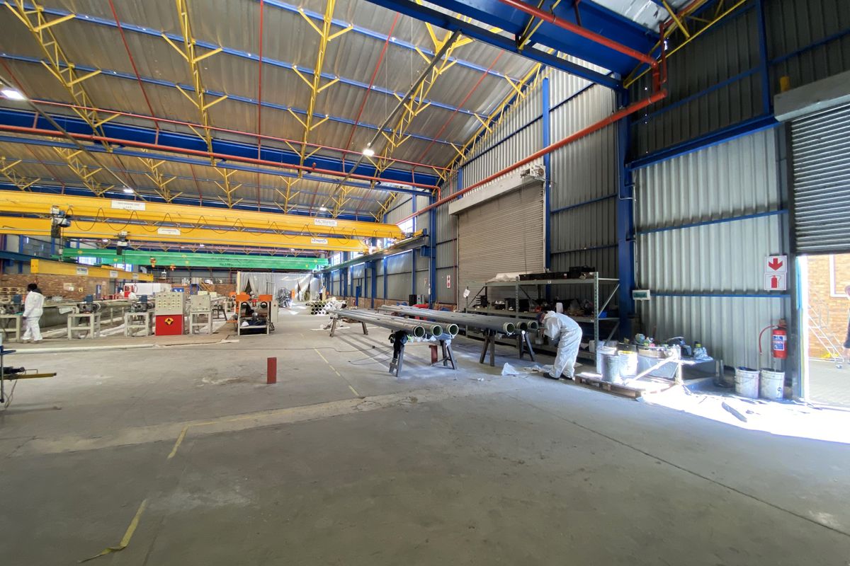 Spacious industrial warehouse facility featuring high-clearance steel truss roofing, overhead gantry cranes, concrete flooring, and large roller shutter access doors.